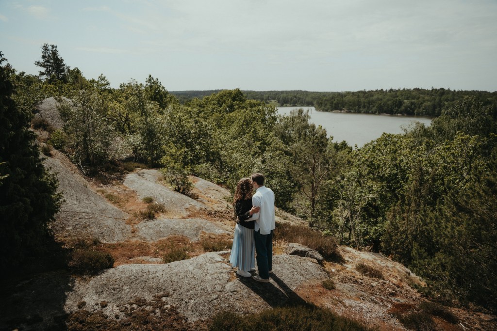Par som står nära varandra på en klippa i en skog framför en sjö
